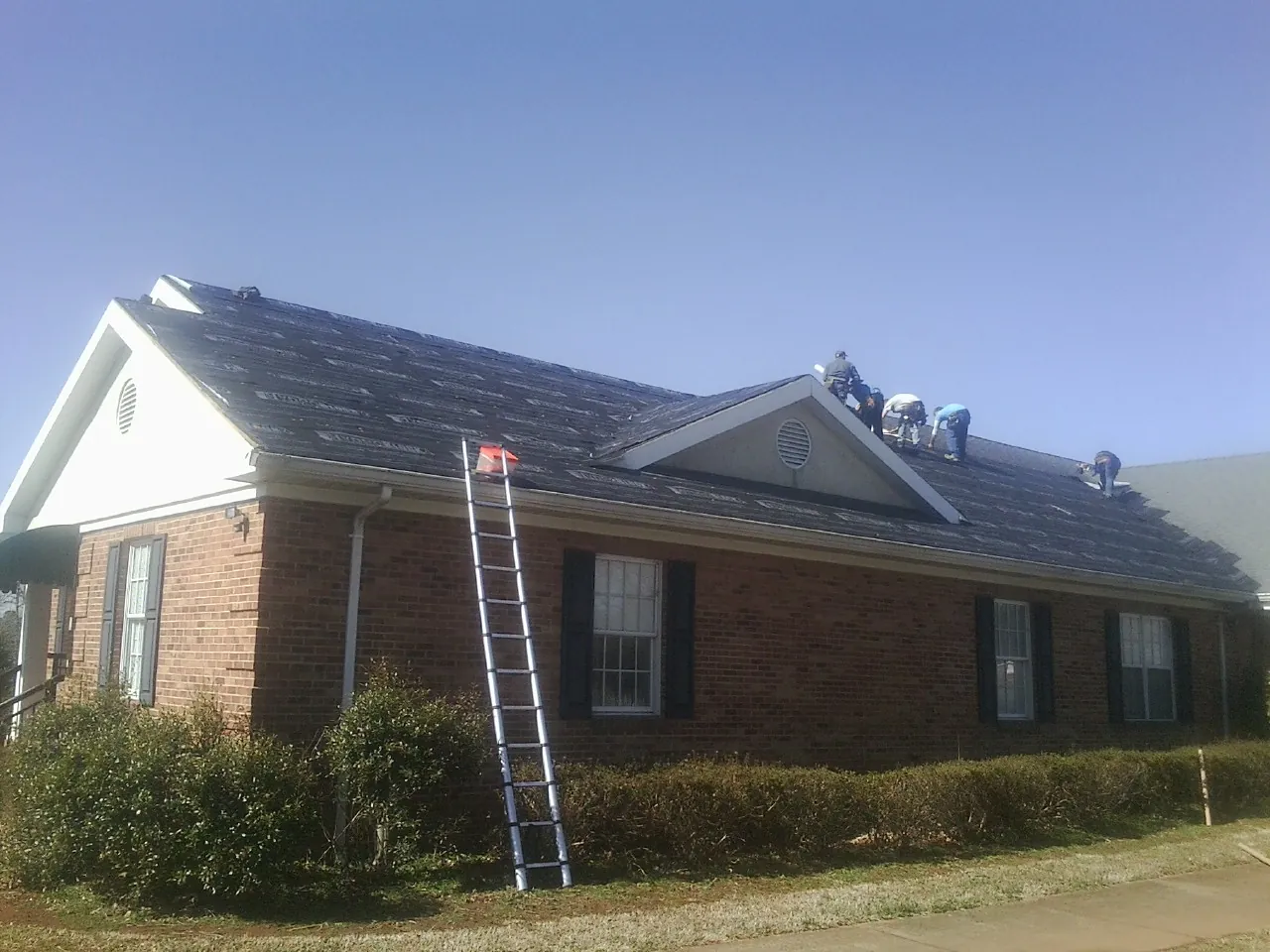Crew tearing shingles off a brick ranch roof with a ladder set — Emergency Roof Repair work by our crew in Gallatin
