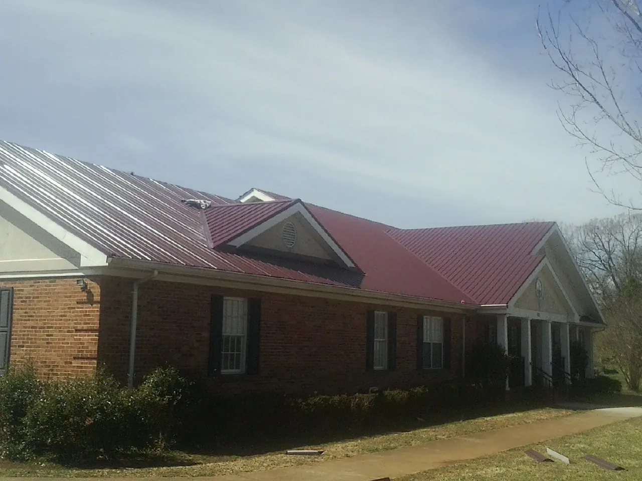 Red metal roof with gabled entries on a long brick building, from a Hail Damage Roof Repair job in Gallatin