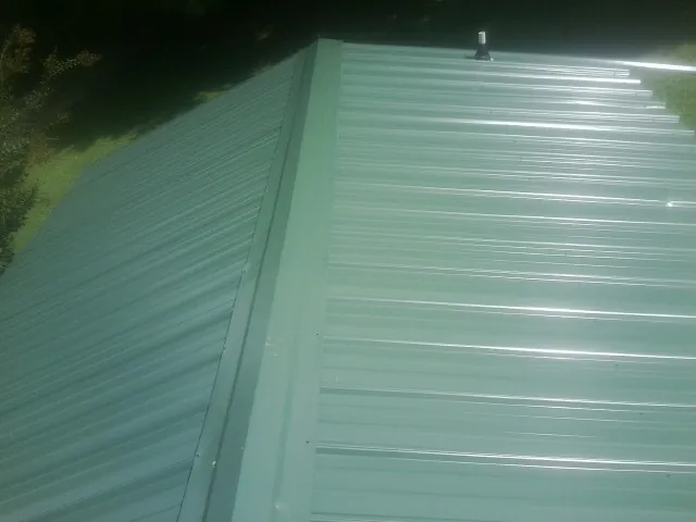 New green metal panels meeting at the ridge of a roof — Flat Roof Repair work by our crew in Gallatin