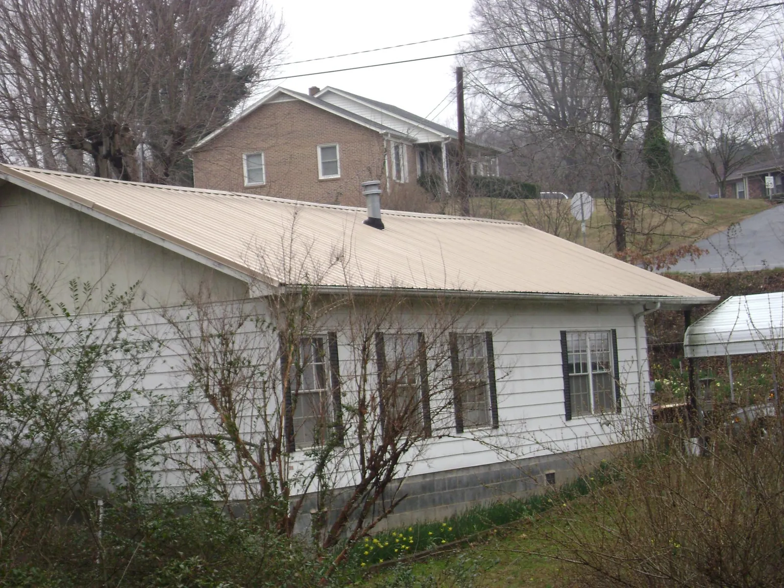 Tan metal roof on a white sided house set into a hillside — Commercial Roofing by Roofing Brothers in Gallatin